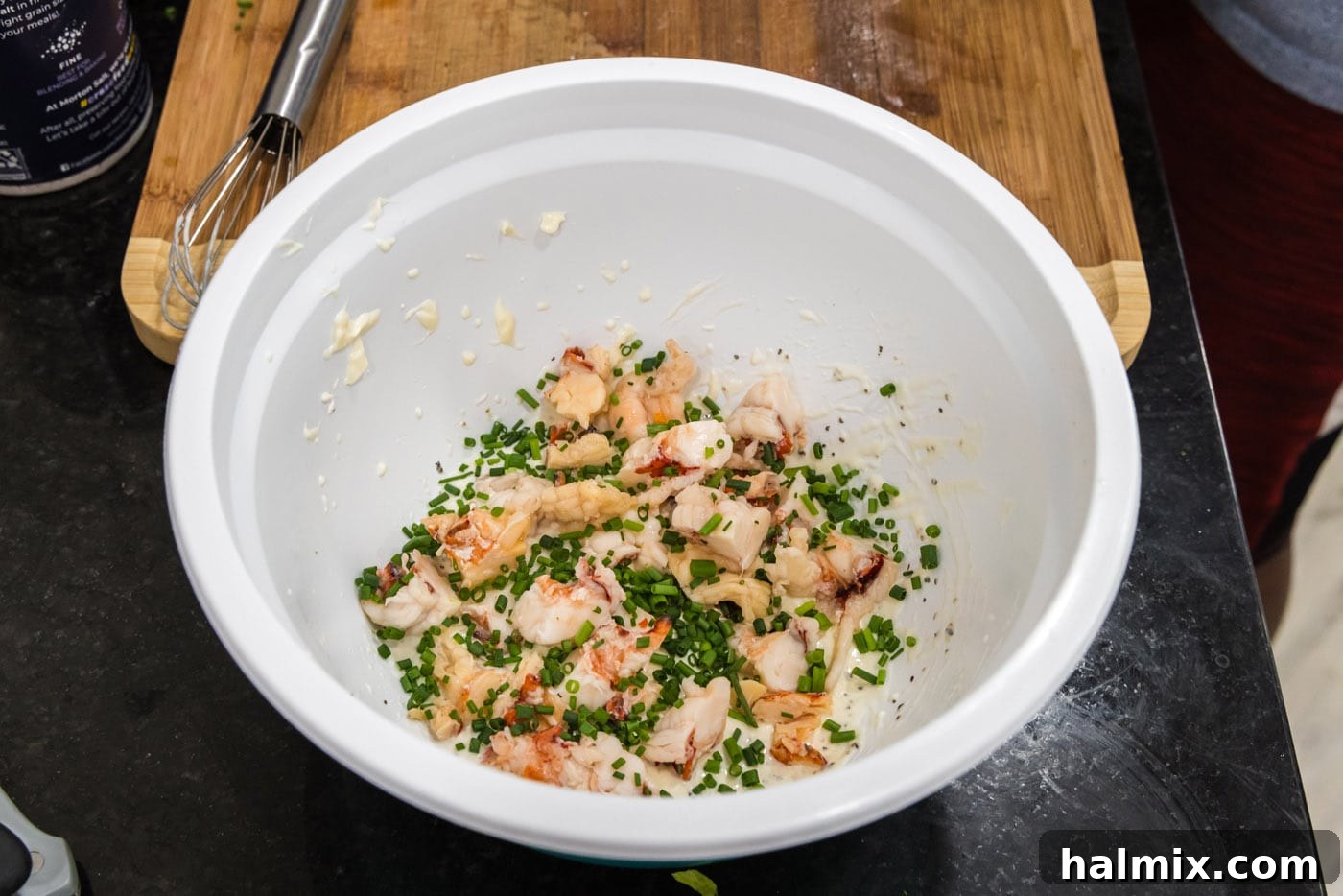 Freshly chopped chives being added to the bowl with cooked lobster meat and creamy dressing.