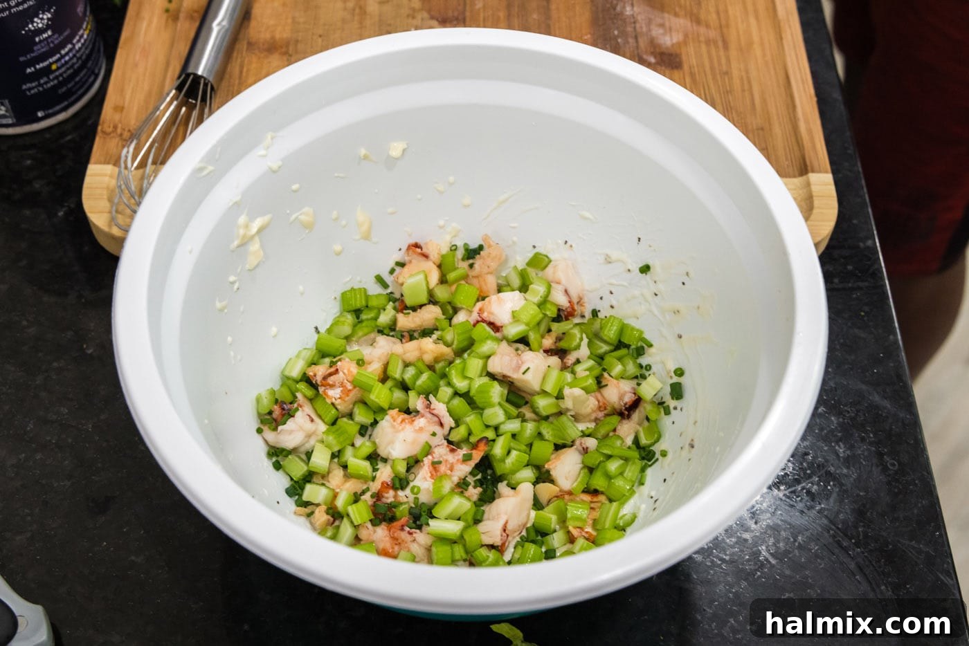Diced celery pieces being carefully added to the mixing bowl containing lobster and dressing.