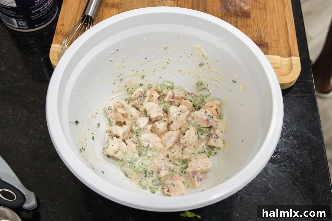 The fully mixed lobster salad in a large mixing bowl, showing the creamy dressing coating the lobster, celery, and chives.