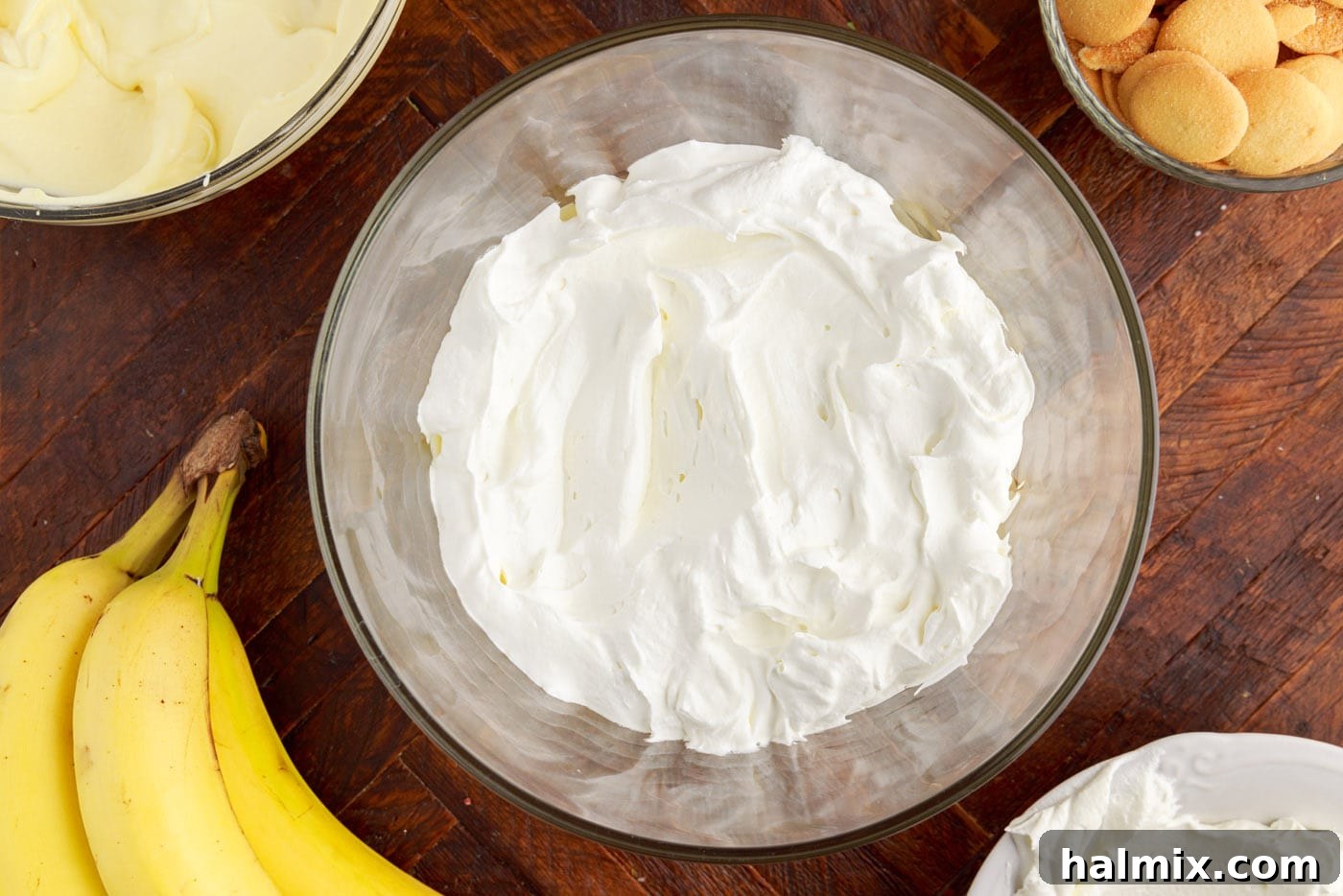 A layer of whipped cream spread over the banana pudding in a trifle bowl.