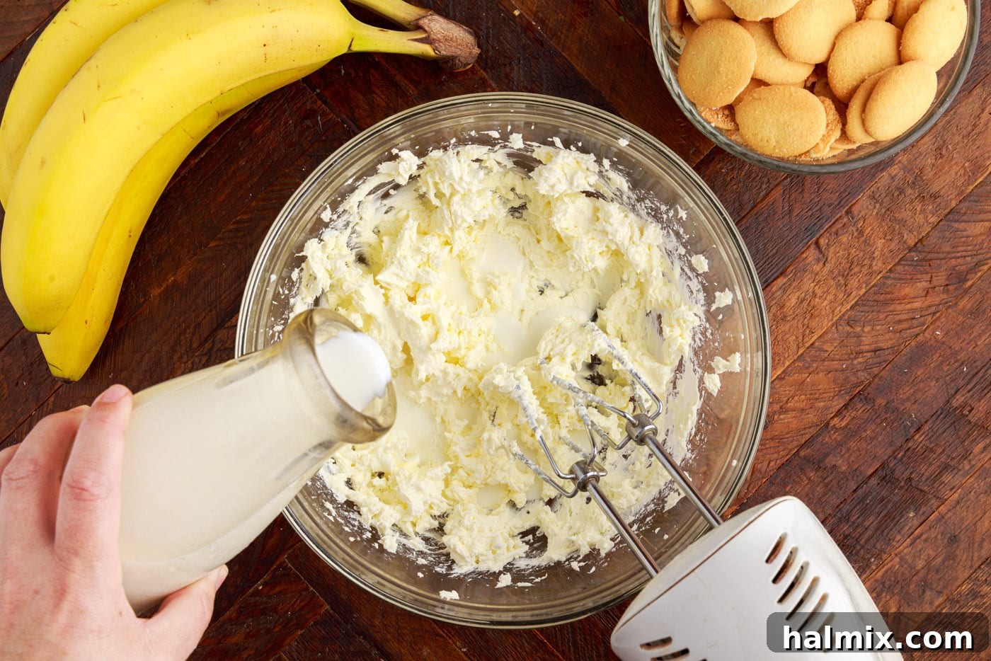 Adding whole milk to softened cream cheese in a bowl and mixing with an electric mixer.