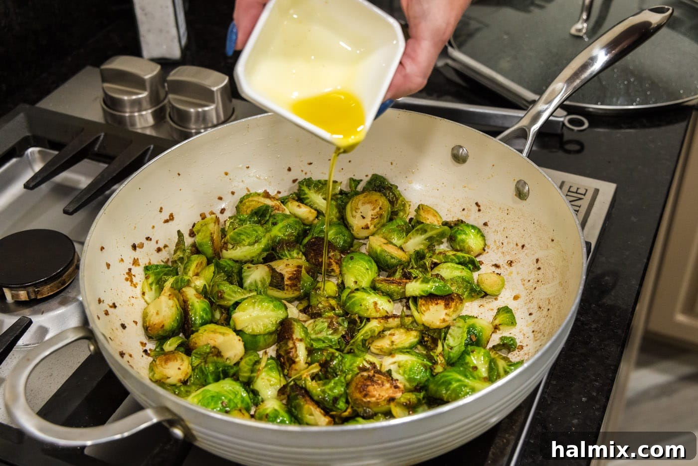 pouring oil into brussels sprouts in a skillet, preparing for final cooking stage