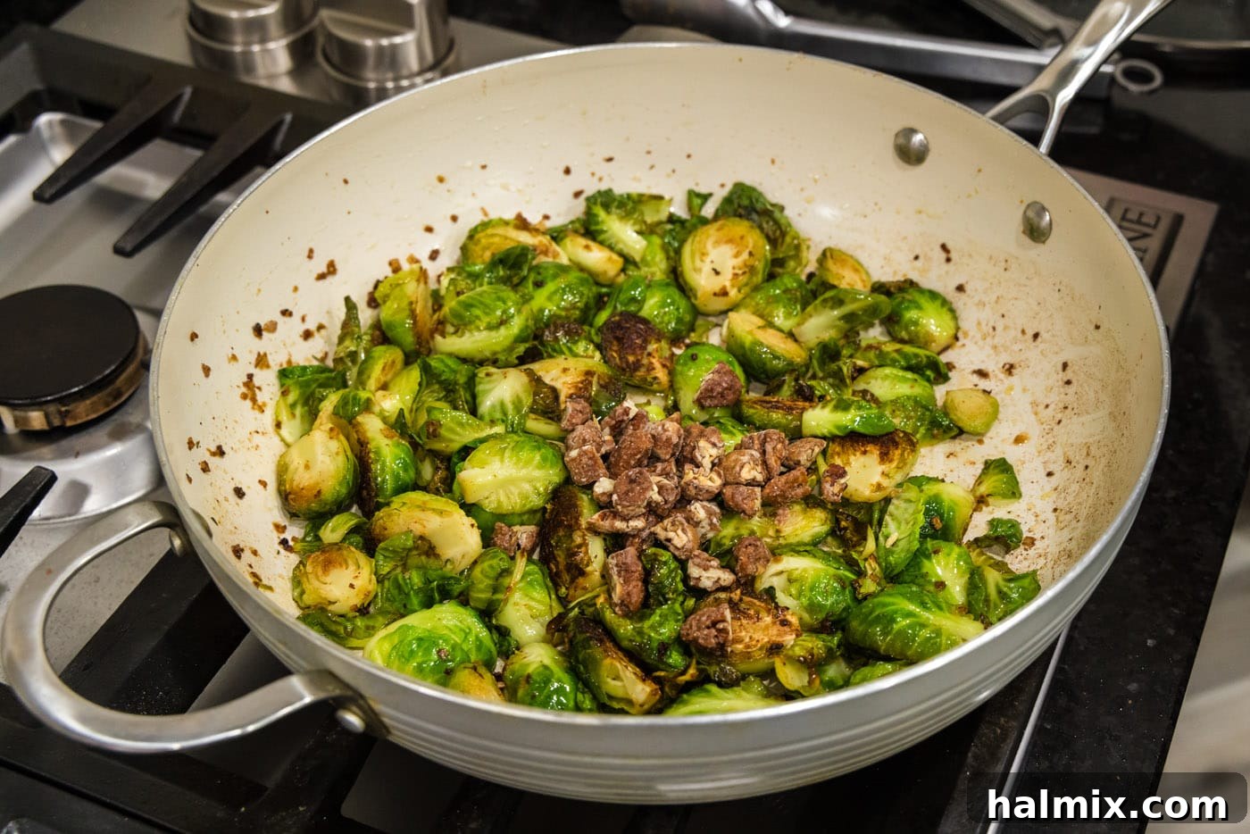candied pecans mixed into brussels sprouts with bacon in a skillet