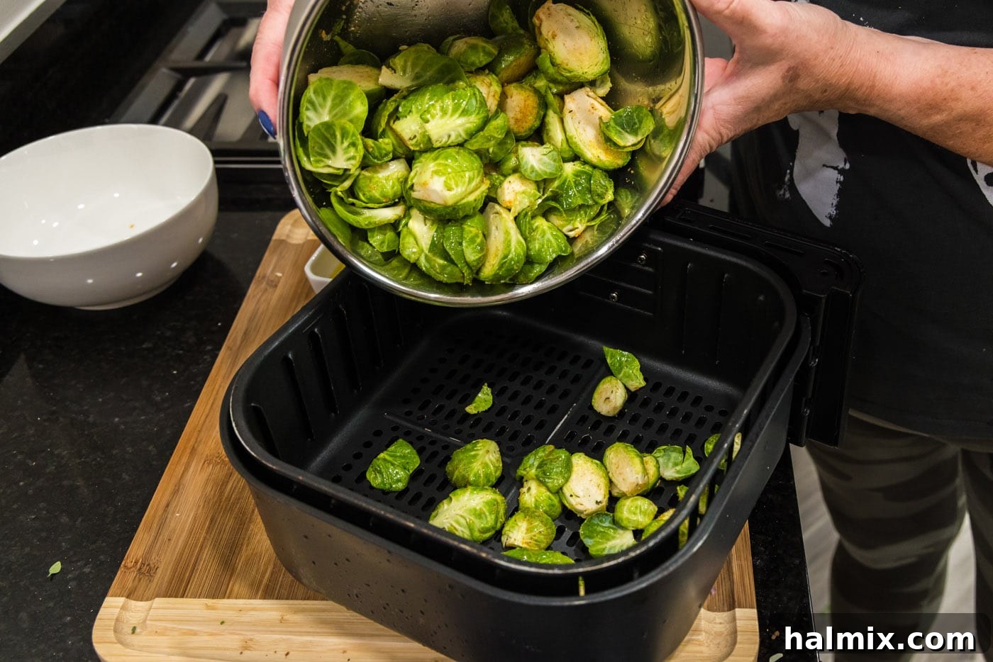 adding brussels sprouts to an air fryer basket, demonstrating the initial cooking step