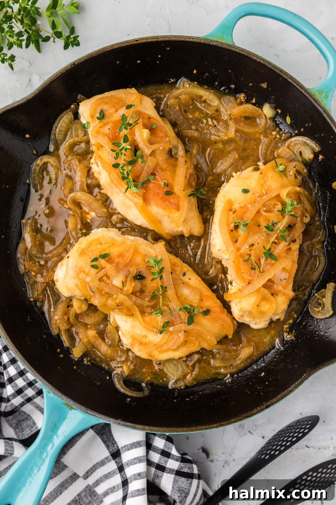 Skillet of perfectly cooked chicken with a rich onion thyme sauce, garnished with fresh thyme sprigs.