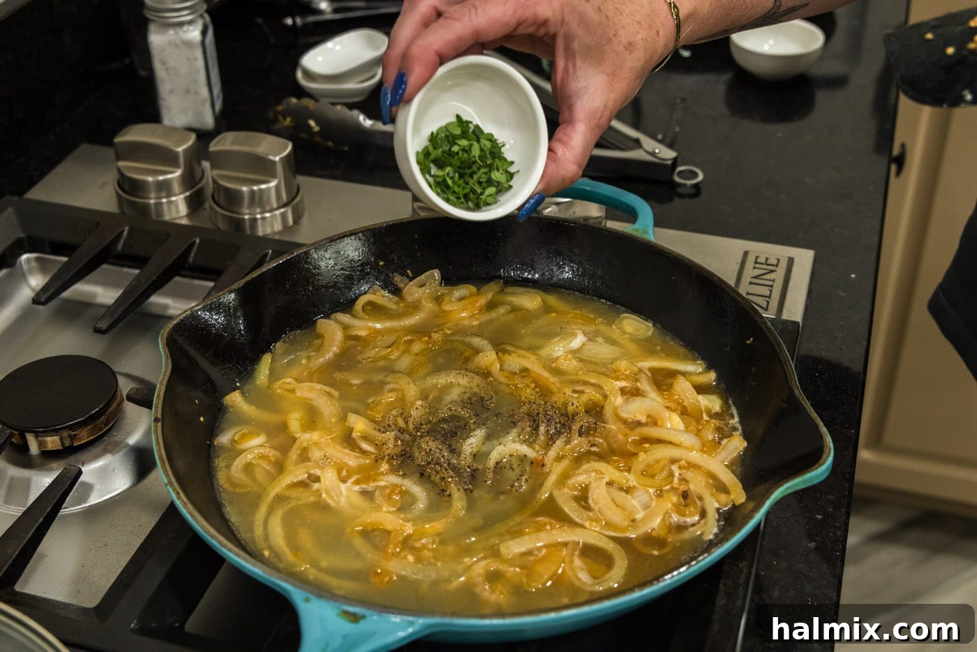 Fresh thyme leaves being added to the simmering onion sauce