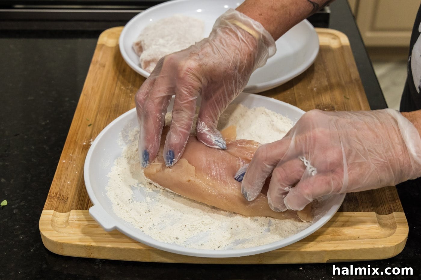 Pressing chicken breasts into flour mixture for coating