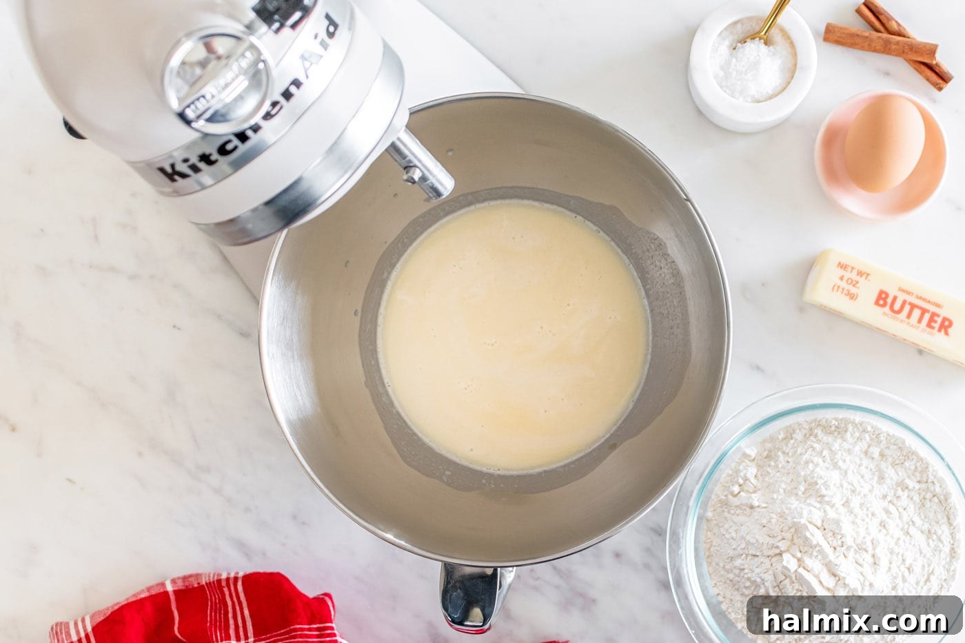 Milk and butter mixture being added to the active yeast in a stand mixer bowl.