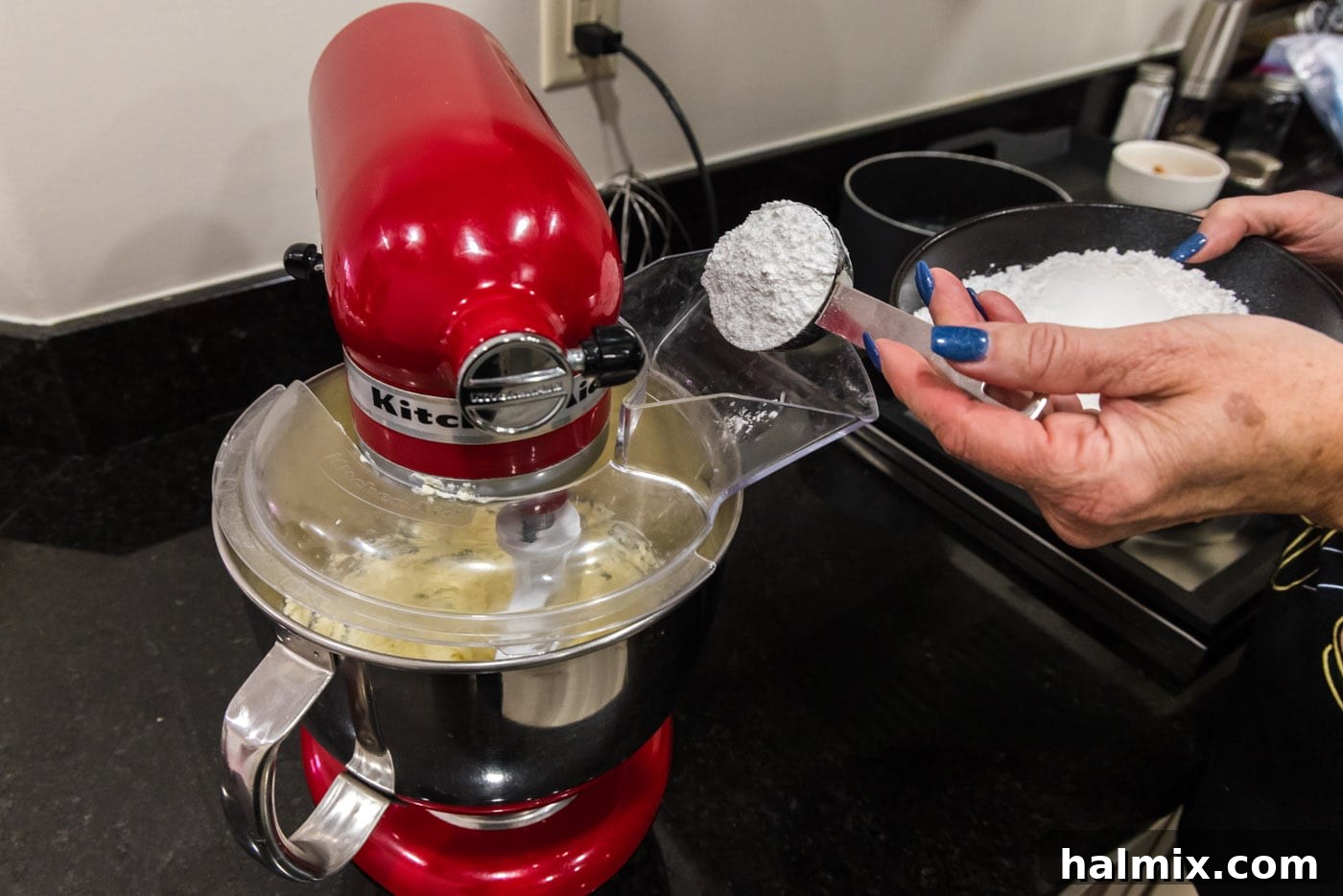 Powdered sugar being gradually added to the butter and cream cheese mixture in a stand mixer