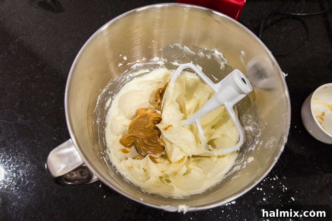 Creamy peanut butter being added to the light and airy cream cheese frosting in a stand mixer bowl