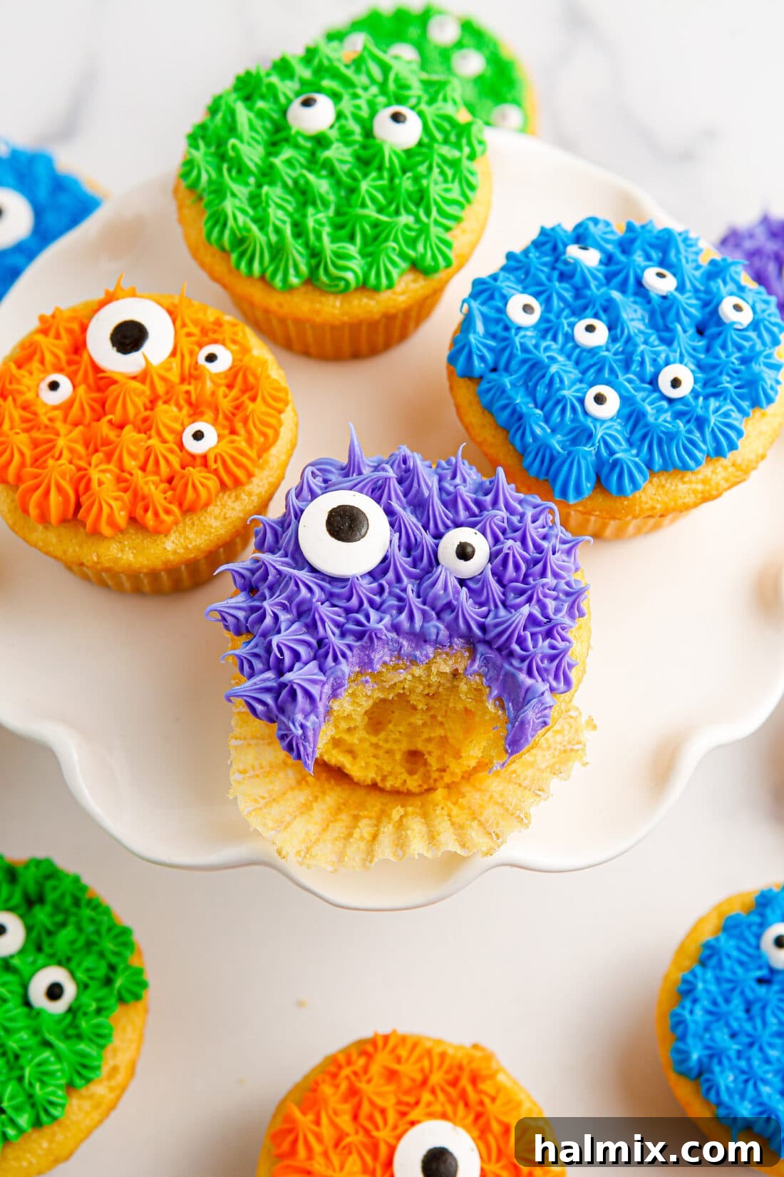 Monster Cupcakes on a cake stand with a bite taken out of one, showcasing vibrant frosting and candy eyeballs