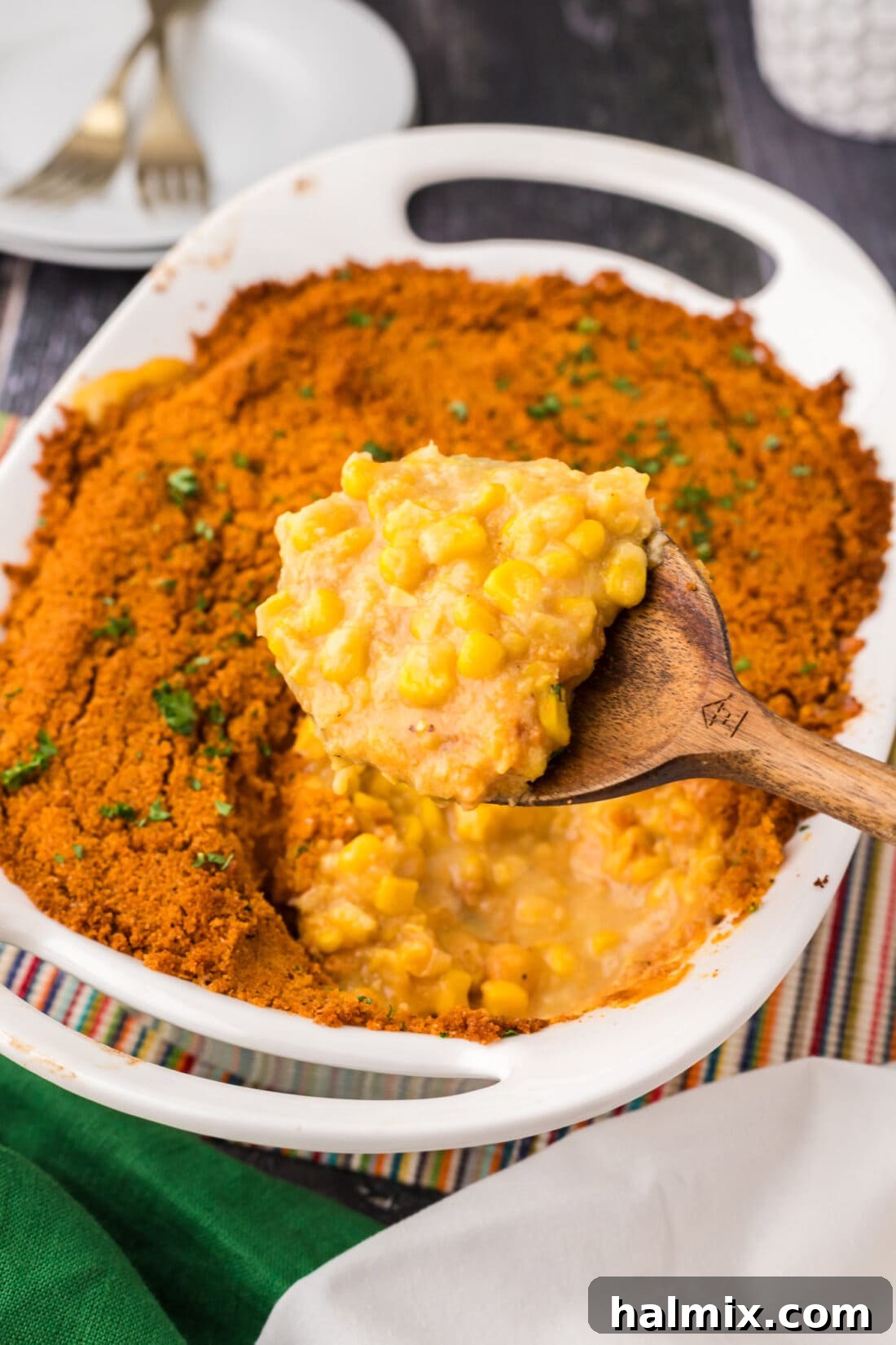 Golden Comfort Corn Bake 2 A spoonful of golden-baked scalloped corn with a crispy cracker topping being lifted from a baking dish, ready to be served.