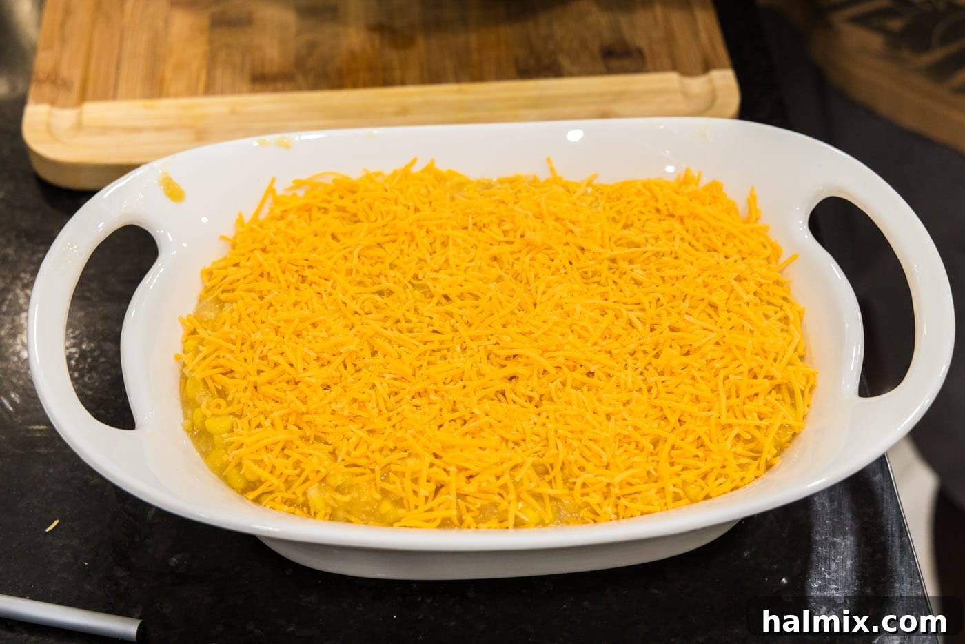 Golden Comfort Corn Bake 12 A generous layer of shredded cheese being sprinkled over the scalloped corn casserole before the final topping is added.