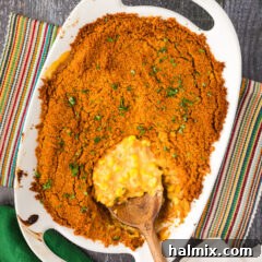 Golden Comfort Corn Bake 16 A spoon removing Scalloped Corn from a baking dish, showcasing its cheesy, creamy texture and crispy topping.