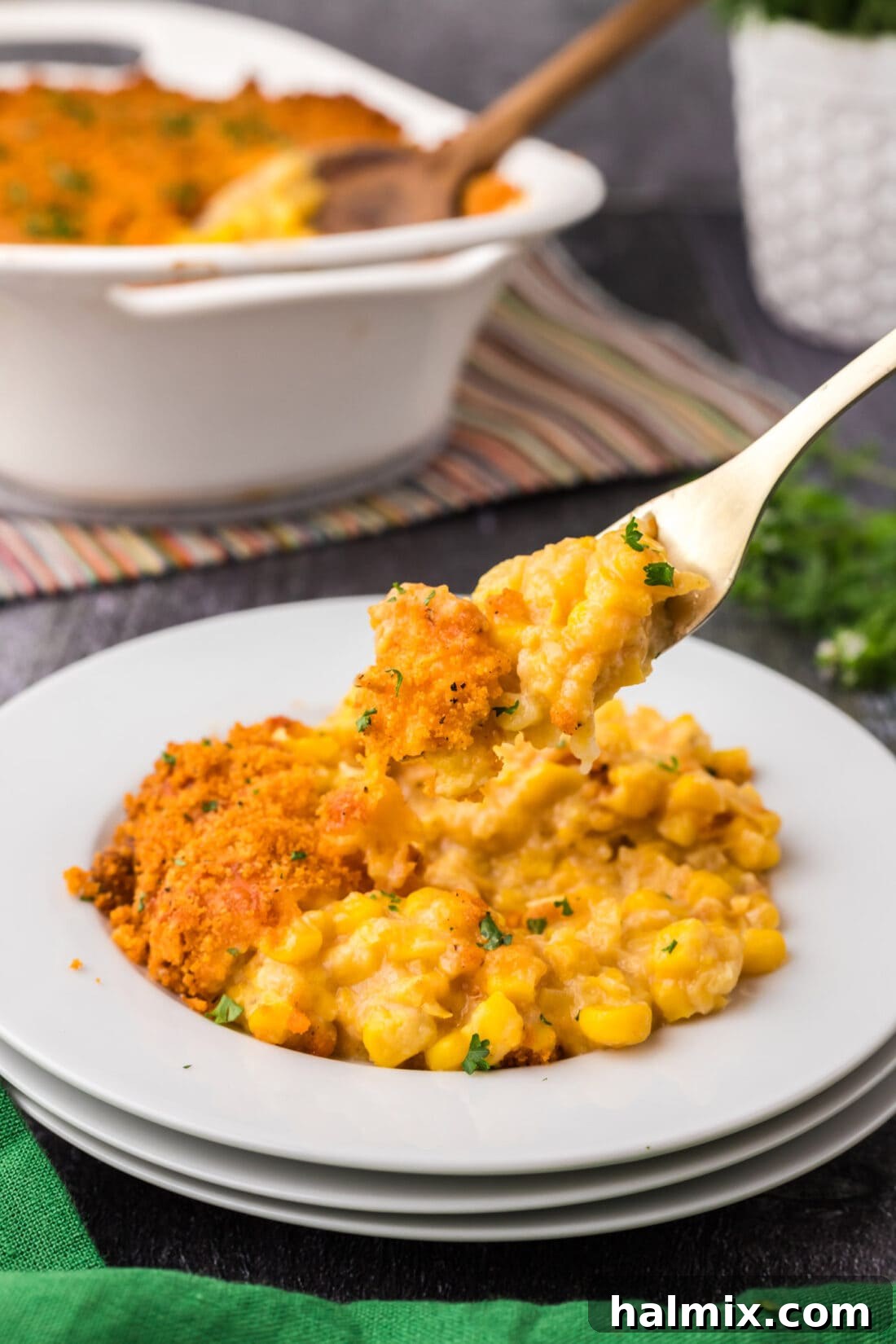 Golden Comfort Corn Bake 3 A forkful of Scalloped Corn, rich with cheese and crispy cracker topping, being lifted from a plate, highlighting its delicious texture.