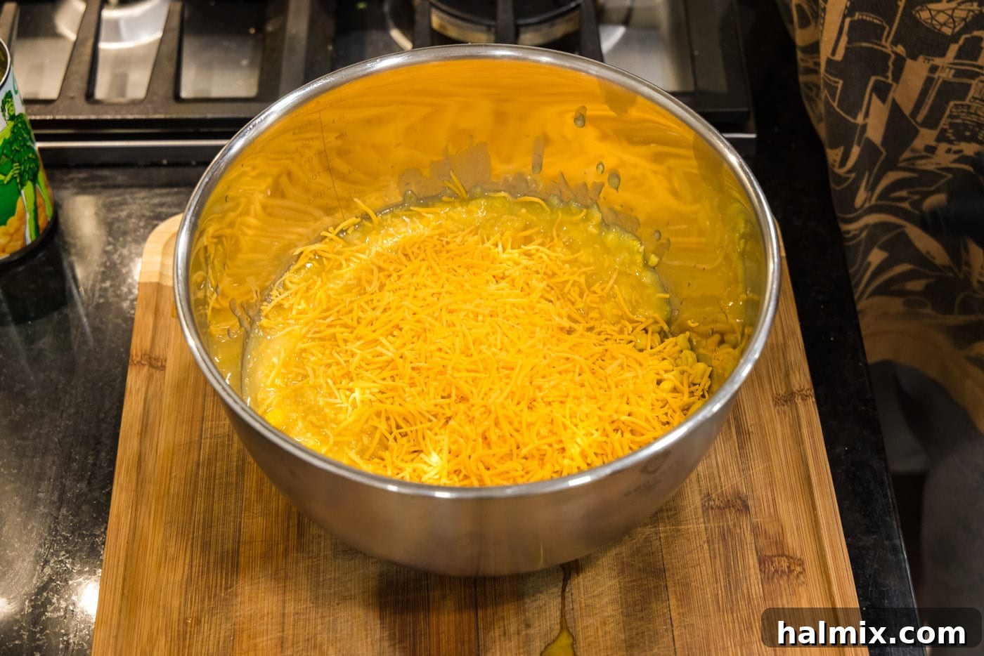 Golden Comfort Corn Bake 9 Shredded cheddar cheese being added to the corn mixture in a mixing bowl, enhancing the savory flavor.