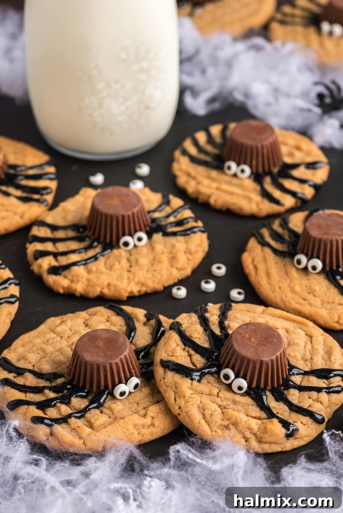 A platter of spooky but sweet spider cookies, with a jar of milk subtly blurred in the background, ready for a Halloween party.