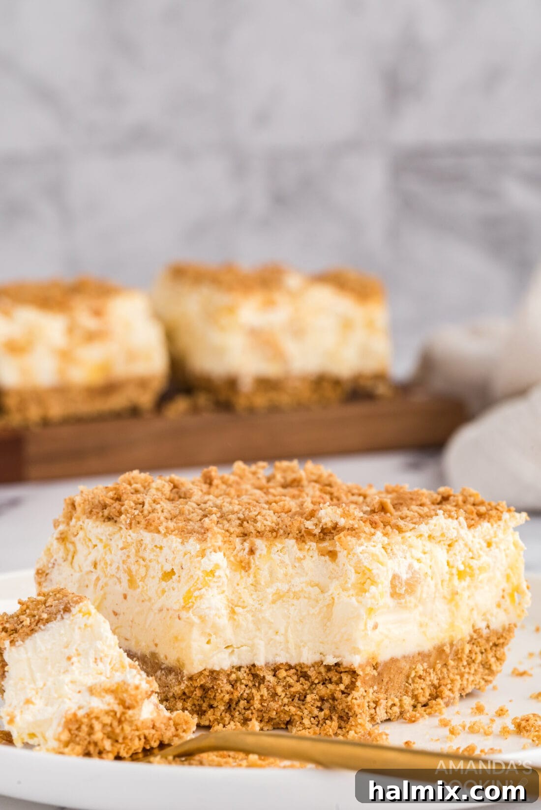 Pineapple Dream Dessert: Cream Cheese, Pineapple, Whipped Cream, Graham Crackers A delectable slice of Pineapple Dream Dessert with a single bite removed, showcasing its creamy layers.