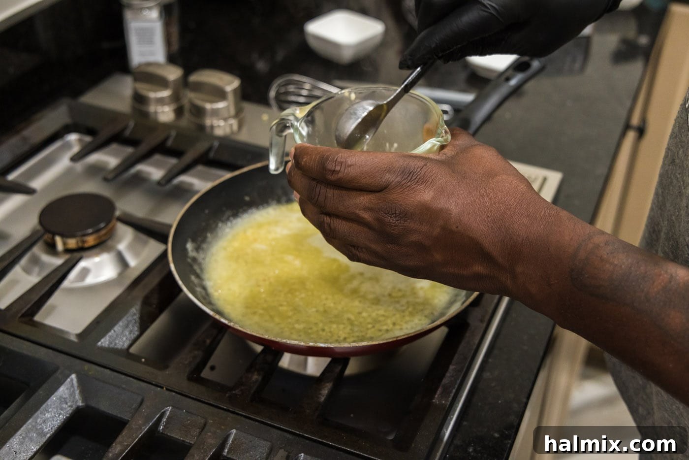 A small measuring cup containing a cornstarch slurry being poured into the skillet of garlic butter sauce for thickening.