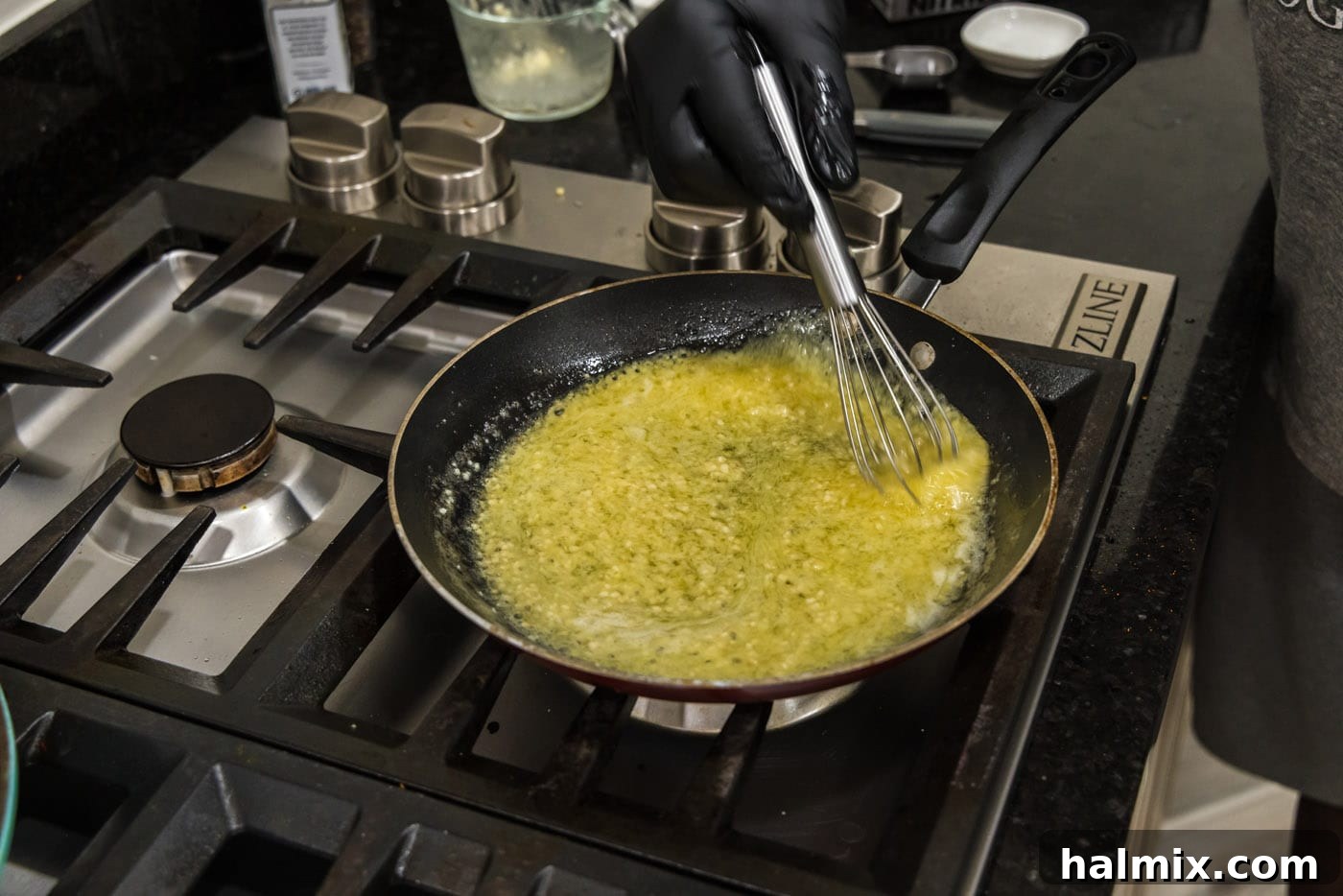 Whisking the garlic butter sauce in a skillet as it thickens and bubbles, creating a smooth, rich texture.