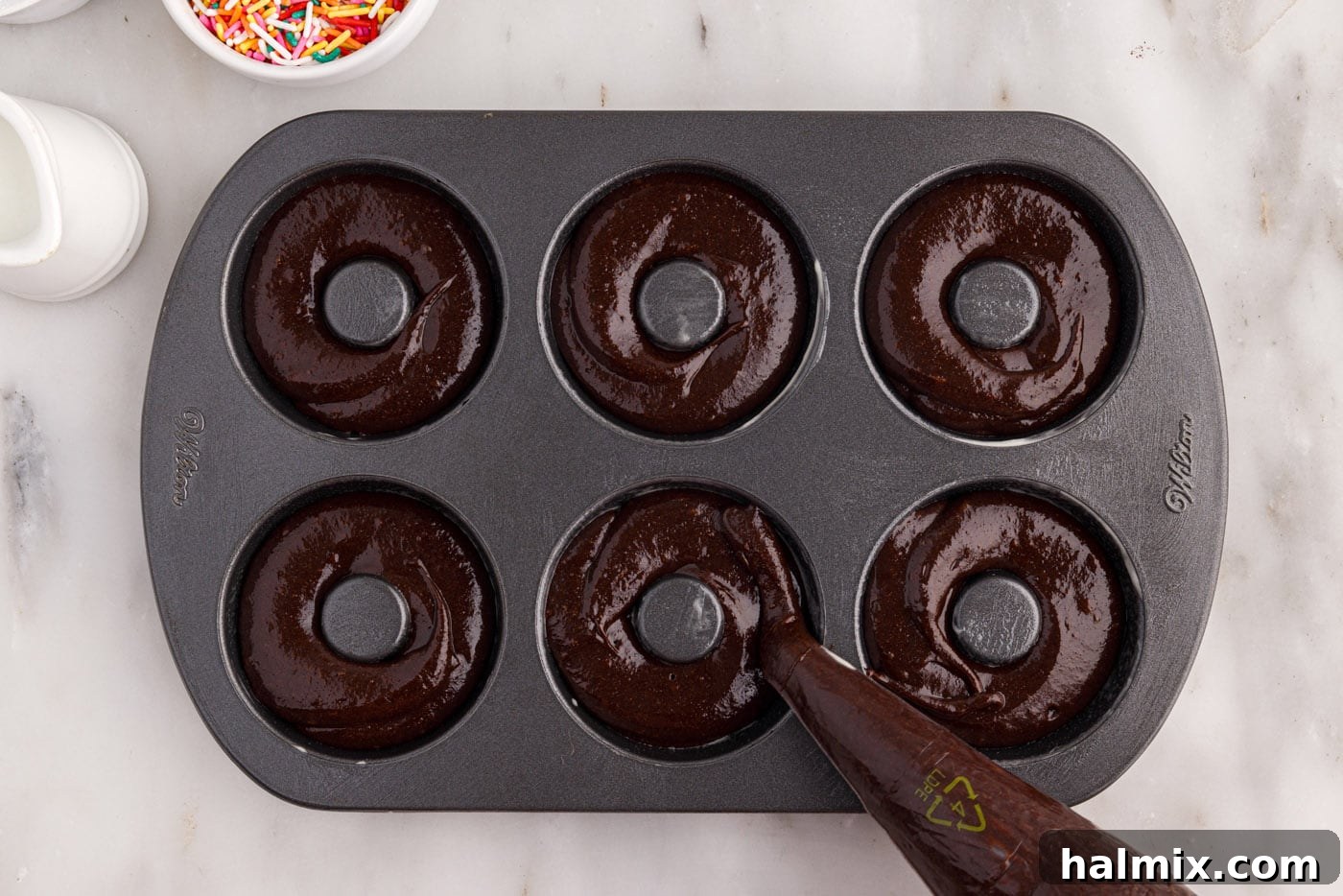Piping bronut batter evenly into the donut pan cavities