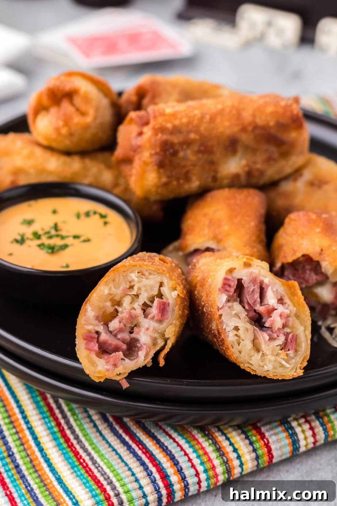 Crispy Reuben Egg Rolls 2 Close up photo of golden brown Reuben Egg Rolls on a plate with a bowl of thousand island dressing, showcasing their crispy texture.