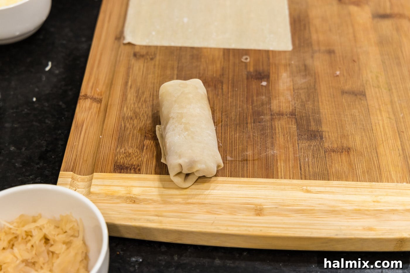 A finished, neatly rolled Reuben egg roll resting on a cutting board, ready for frying.