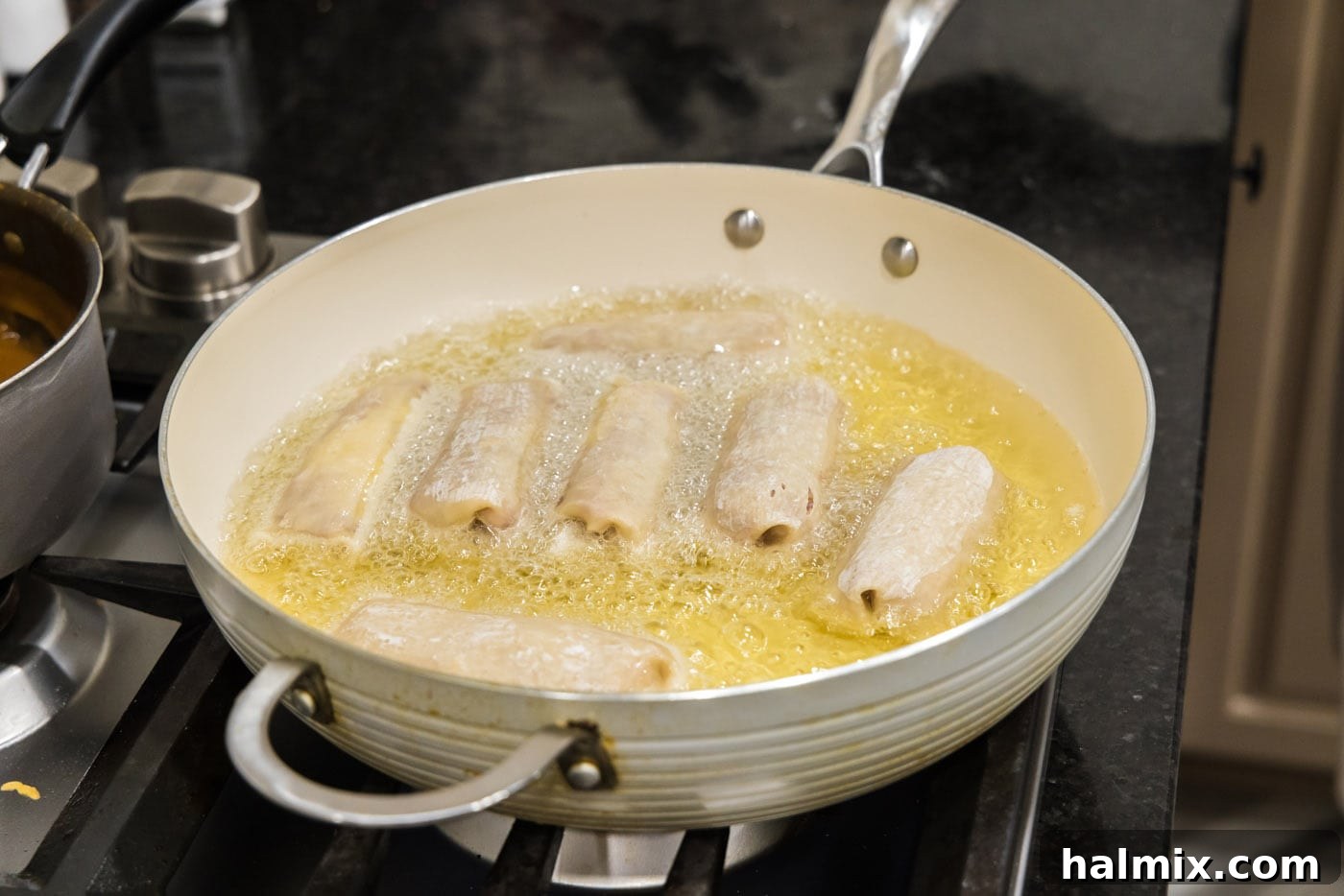 Crispy Reuben Egg Rolls 10 Several Reuben egg rolls sizzling and turning golden brown in hot oil within a deep-sided skillet, halfway through frying.