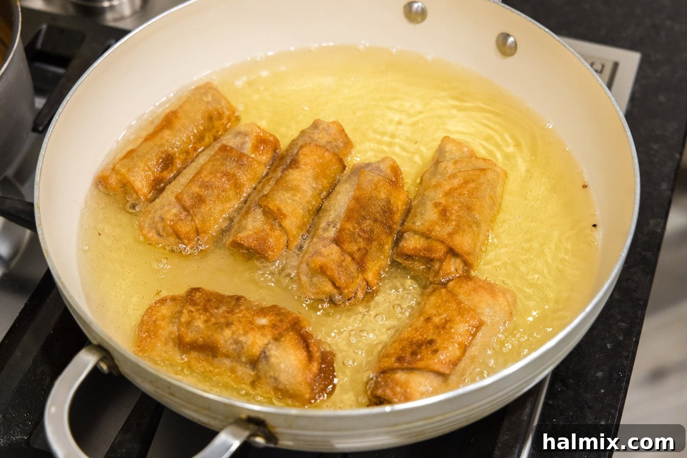 Crispy, golden-fried Reuben egg rolls cooking in a skillet, showcasing their perfect browning and bubbling oil.