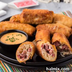 Close up photo of a Reuben Egg Roll cut in half on a plate with more rolls in the background, showing the delectable filling.