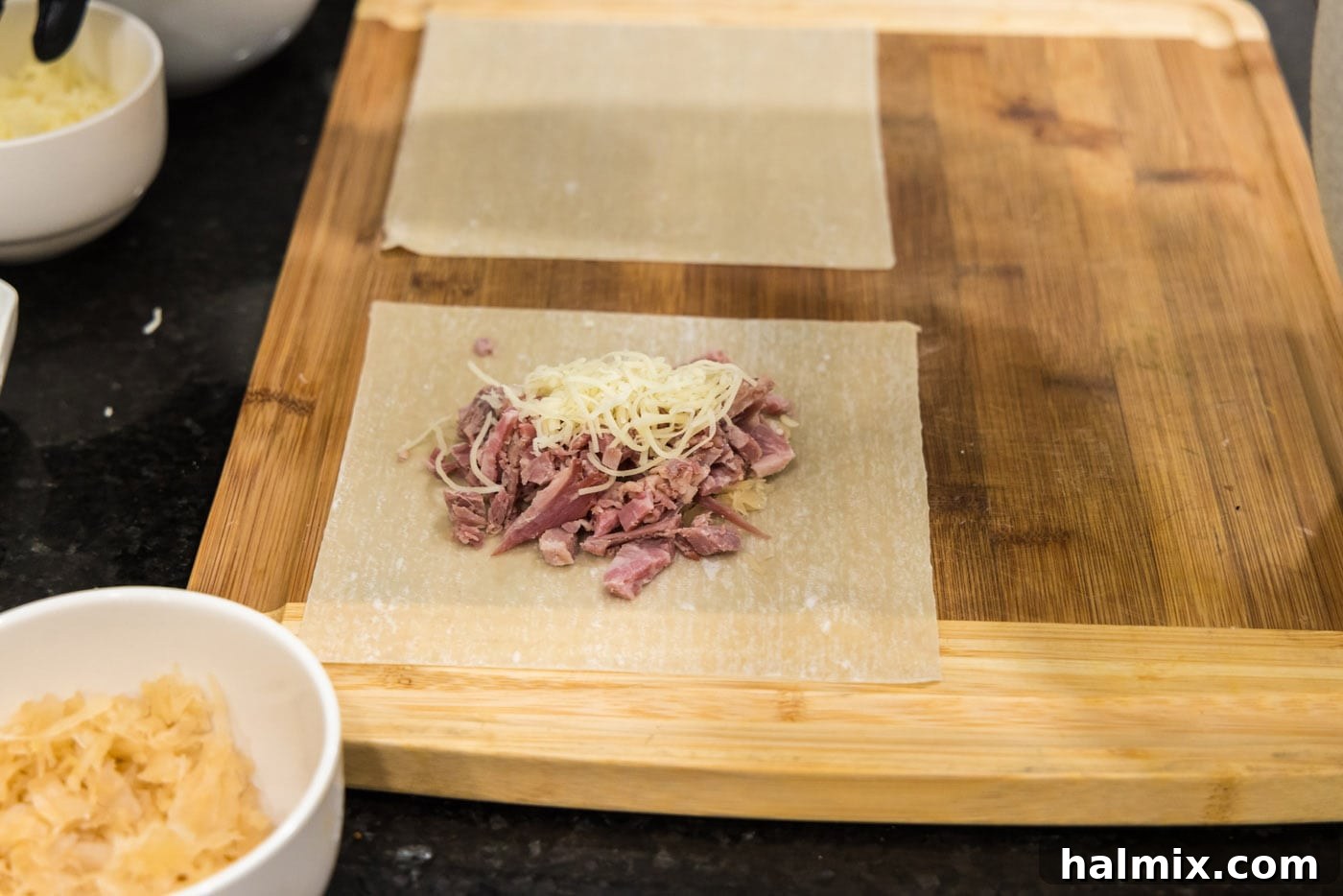 An egg roll wrapper showcasing chopped corned beef layered over sauerkraut, topped with a sprinkle of shredded Swiss cheese, centrally placed for wrapping.