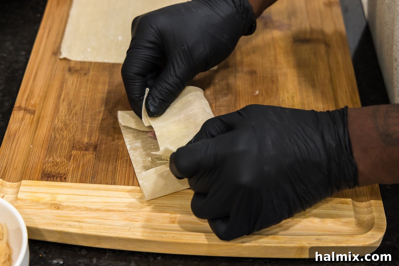 A sequence of three images showing the process of folding and rolling an egg roll wrapper, sealing the edges with water to create a tight, secure roll.