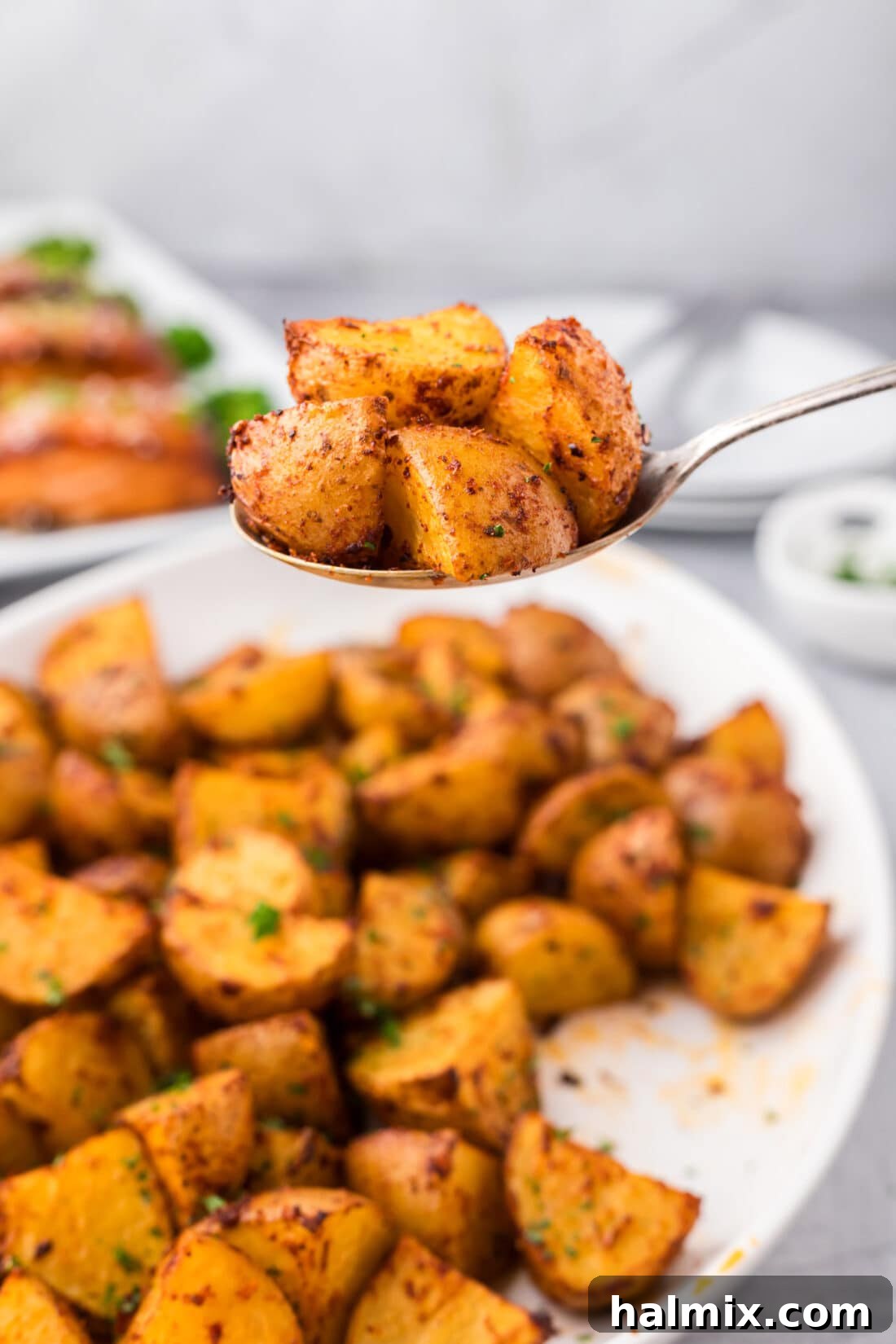 A serving spoon lifting a portion of spicy roasted potatoes, highlighting their golden-brown crust, over a full platter.