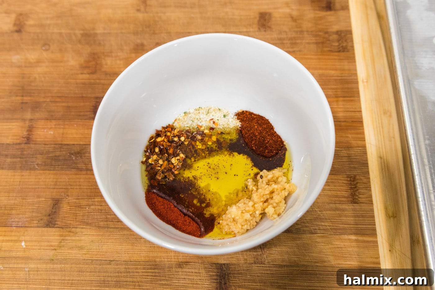 A small bowl holding the vibrant seasoning blend: red pepper flakes, olive oil, minced garlic, cayenne pepper, and chili powder.