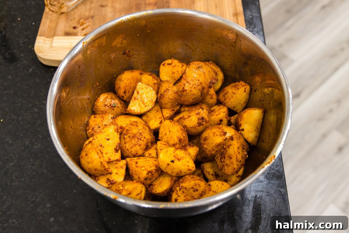 Seasoned spicy roast potatoes glistening in a mixing bowl, perfectly coated and ready for baking.