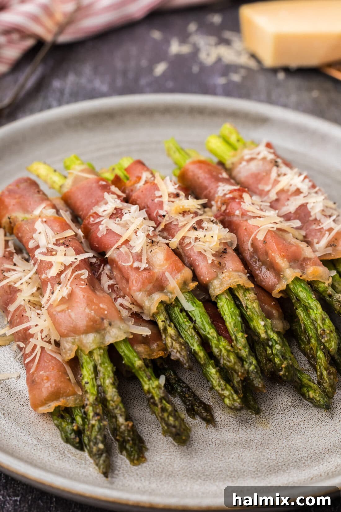 Prosciutto Asparagus Bundles 2 Tender Prosciutto Wrapped Asparagus spears stacked on a white plate, ready to be served, showcasing their golden-brown edges.