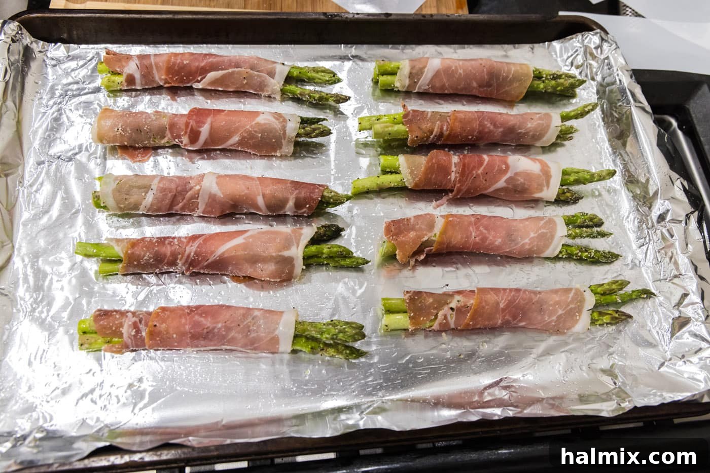 Prosciutto Asparagus Bundles 12 Prosciutto wrapped asparagus bundles neatly arranged on a baking sheet before going into the oven.