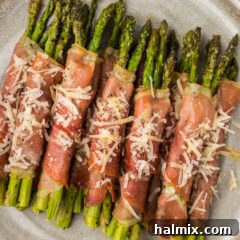 Close up photo of Prosciutto Wrapped Asparagus on a plate topped with shaved parmesan