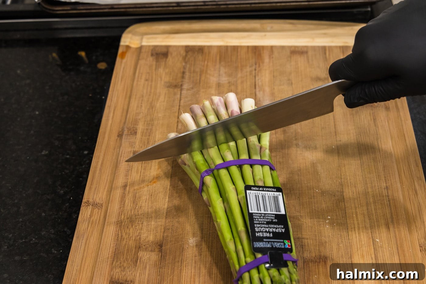 Prosciutto Asparagus Bundles 5 A knife cutting the woody end off an asparagus spear on a cutting board.