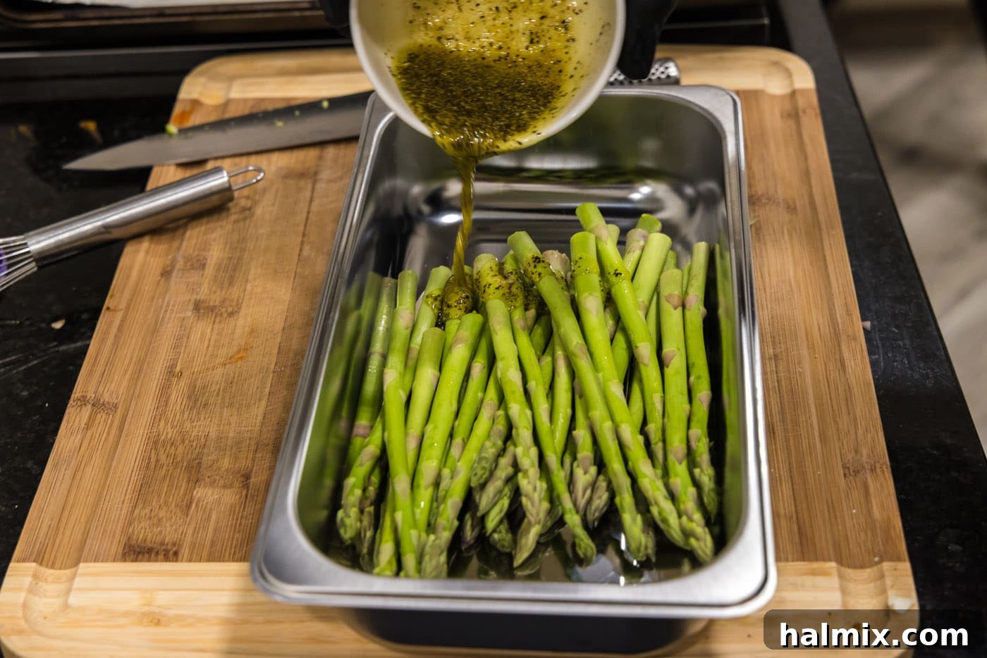 Prosciutto Asparagus Bundles 6 Olive oil and seasoning mixture being poured over asparagus spears in a bowl.