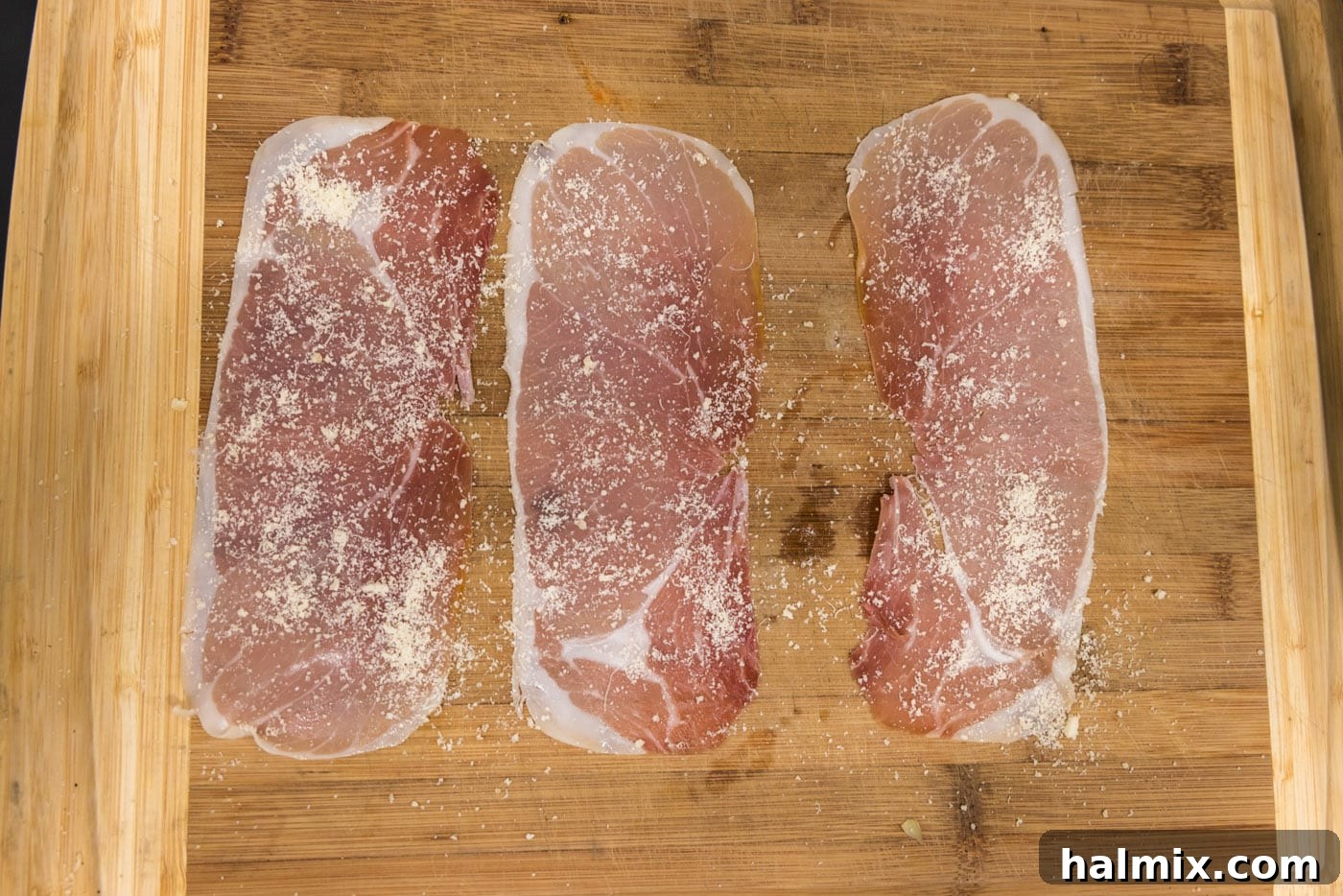 Prosciutto Asparagus Bundles 8 Slices of prosciutto laid out on a cutting board, topped with a sprinkle of grated Parmesan cheese.