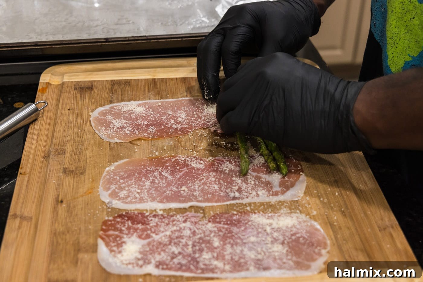 Prosciutto Asparagus Bundles 9 Hands carefully rolling a bundle of asparagus spears in a slice of prosciutto with cheese.
