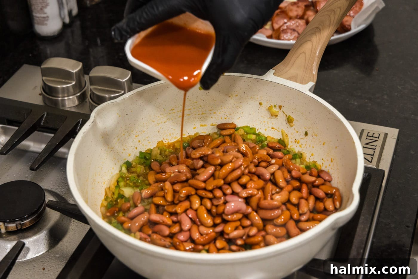 Bayou Red Beans and Rice Legacy 8 hot sauce being poured over red beans and sautéed vegetables in a skillet