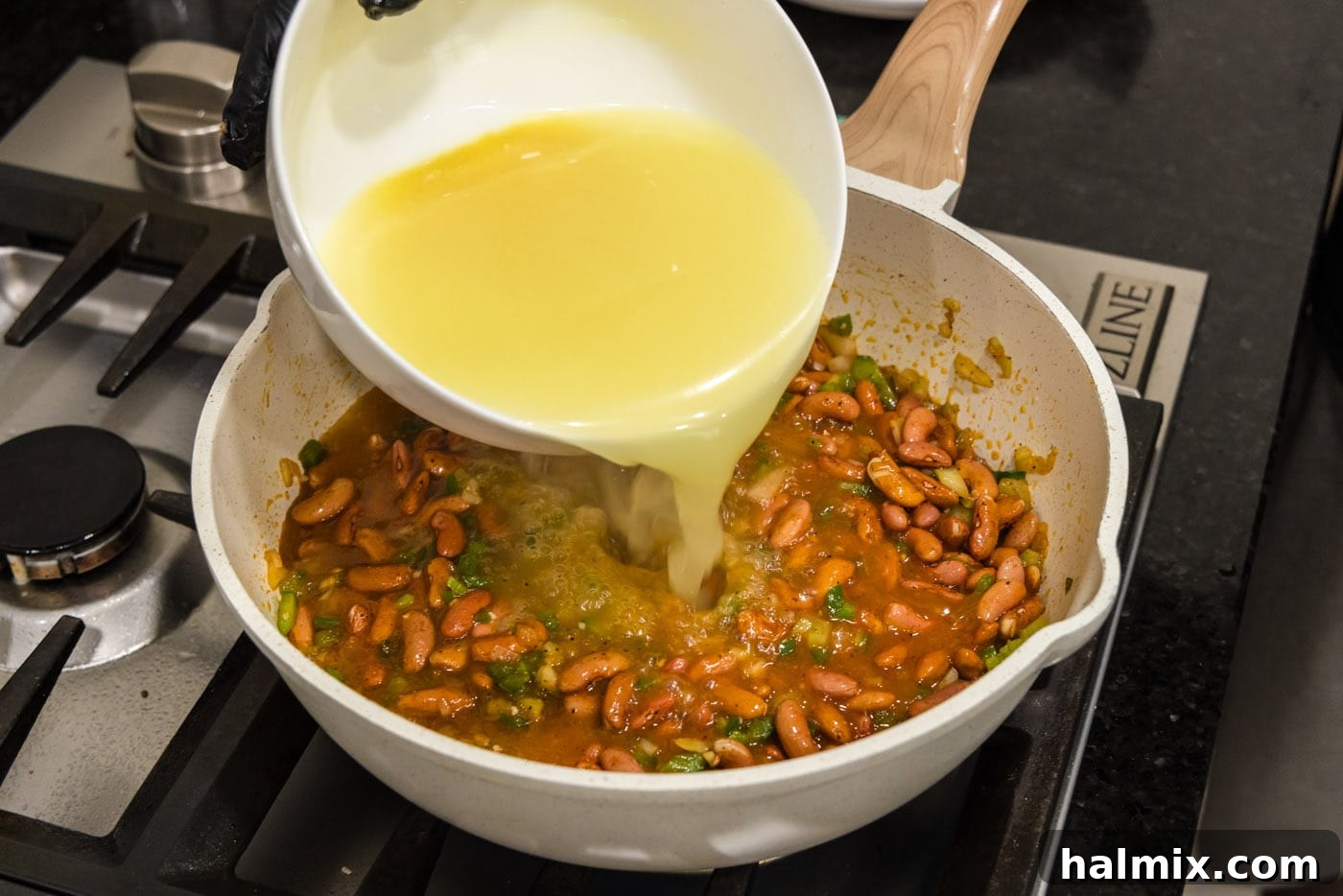 Bayou Red Beans and Rice Legacy 9 chicken broth being added to the red bean and vegetable mixture in a large skillet