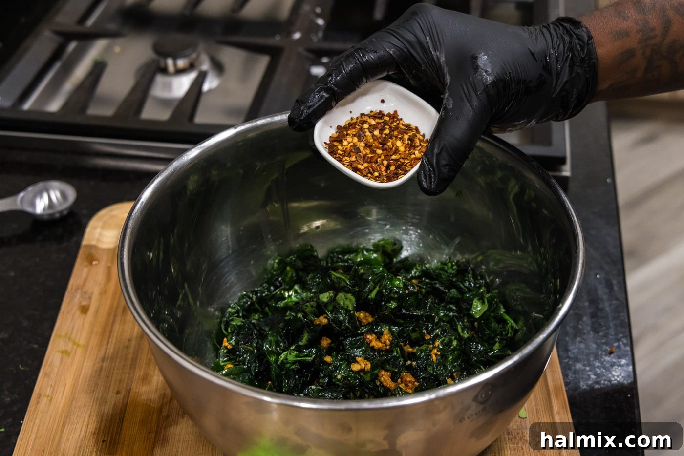 Adding vibrant red pepper flakes to the drained crispy fried spinach and golden garlic, ready for seasoning