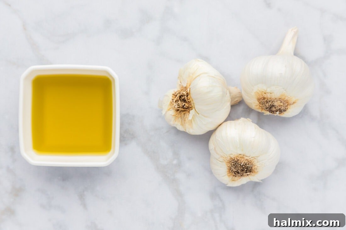 A visual display of the two primary ingredients needed for roasting garlic: fresh whole garlic bulbs and a bottle of high-quality olive oil.