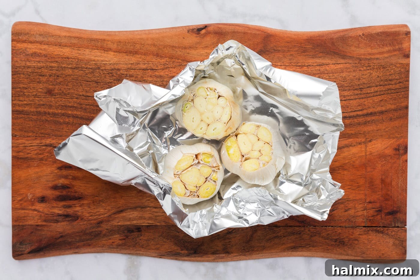 Sliced whole bulbs of garlic arranged in aluminum foil, awaiting the drizzle of olive oil before roasting.