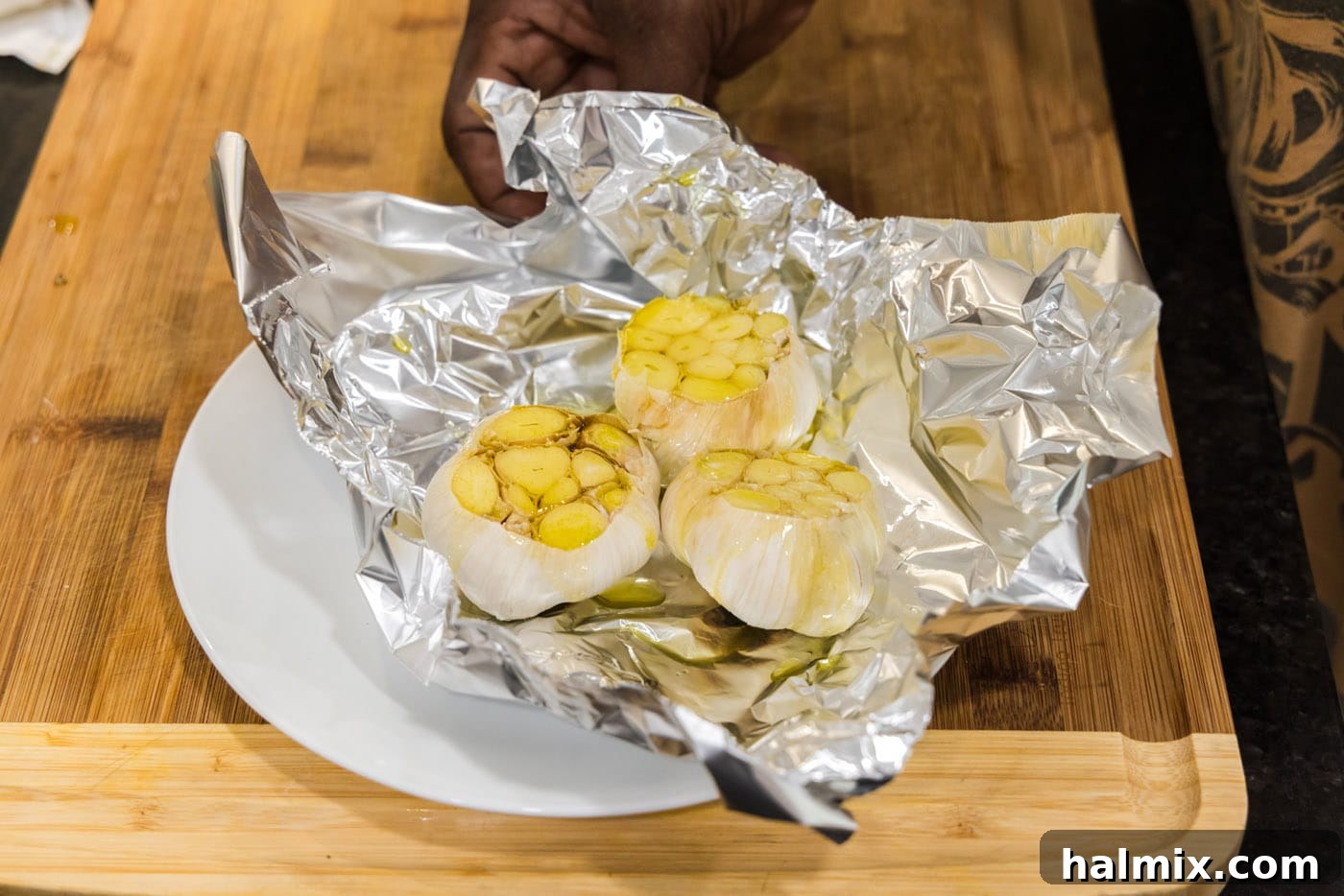 Garlic bulbs in aluminum foil, generously drizzled with olive oil on their exposed cloves, ready to be sealed and roasted.