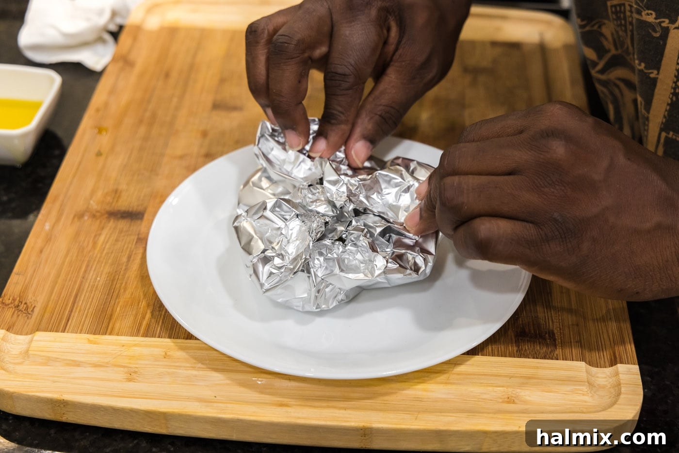A tightly sealed aluminum foil packet enclosing garlic bulbs, placed on a baking sheet and ready for the oven, ensuring tender, roasted garlic.