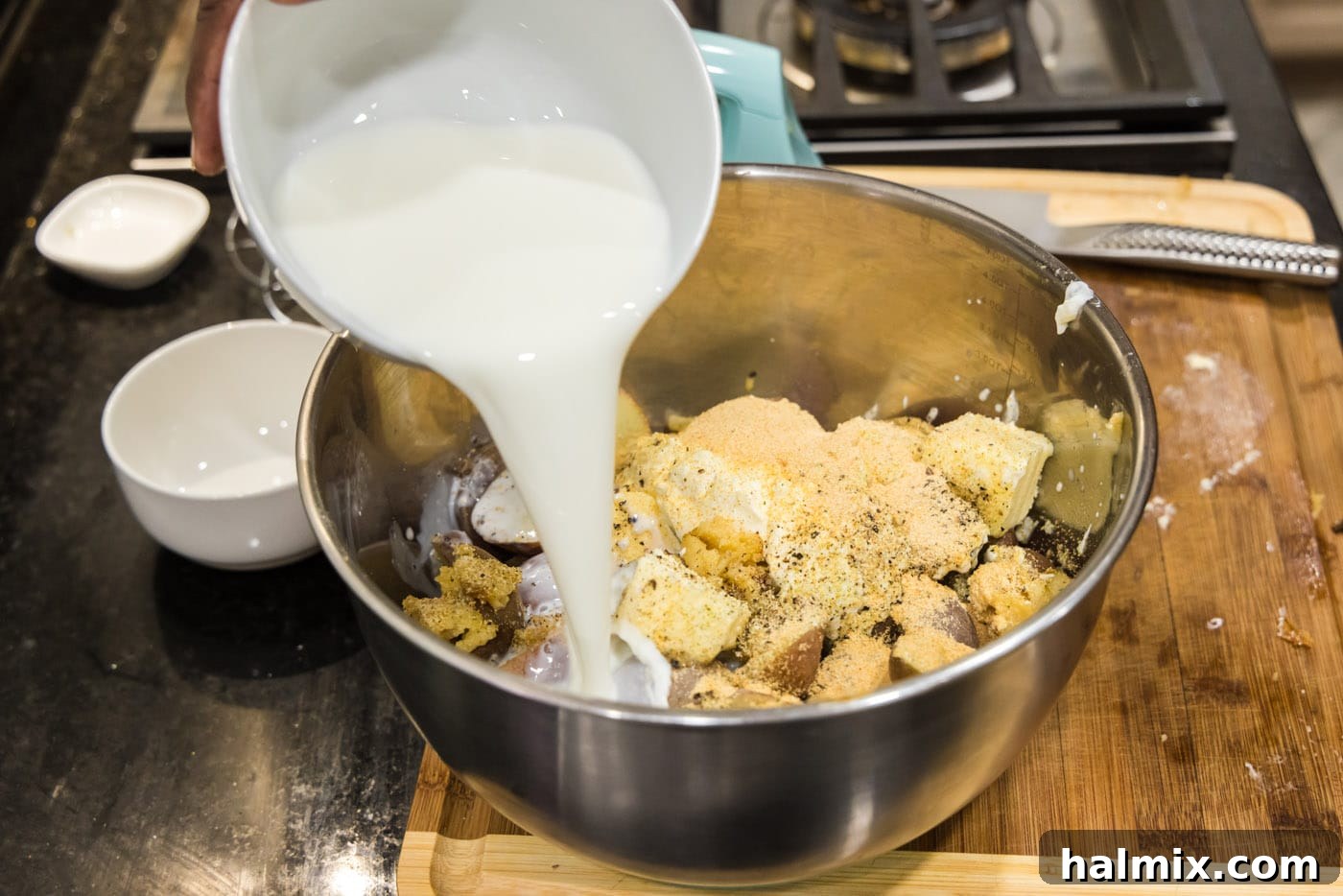 pouring heavy whipping cream into bowl of sour cream, butter, potatoes, and garlic